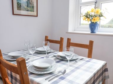 A dining table set with plates glasses and cutlery near a window with flowers in a vase at The Barn - Poplar Farm in Lower Dunsforth near Boroughbridge