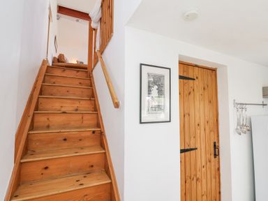 Wooden stairs leading to a living area with a brown sofa a wooden door with black hinges white walls and a framed picture at The Barn - Poplar Farm in Lower Dunsforth near Boroughbridge