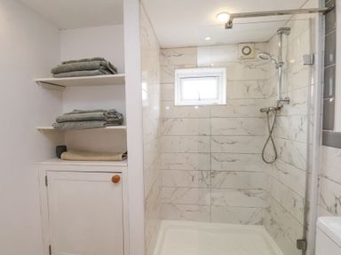 A bathroom with a walk-in shower with a glass door and tiled walls with a window and shelves with folded towels at The Barn - Poplar Farm in Lower Dunsforth near Boroughbridge