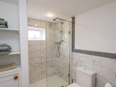 A bathroom with a shower enclosure and shelves with folded towels at The Barn - Poplar Farm in Lower Dunsforth near Boroughbridge