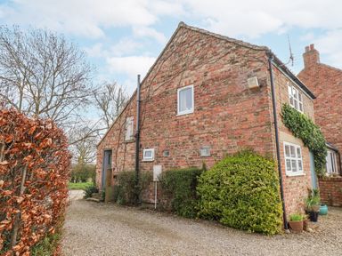 A brick house with small bushes and a gravel driveway at The Barn - Poplar Farm in Lower Dunsforth near Boroughbridge