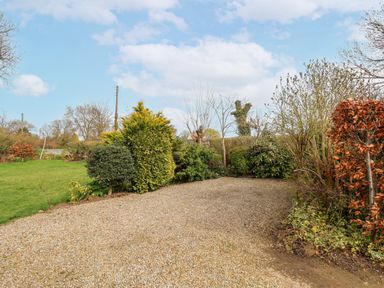 A gravel driveway bordered by bushes and trees next to a grass lawn at The Barn - Poplar Farm in Lower Dunsforth near Boroughbridge