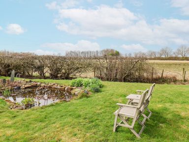 A garden with a small pond and two wooden chairs on grass at The Barn - Poplar Farm in Lower Dunsforth near Boroughbridge