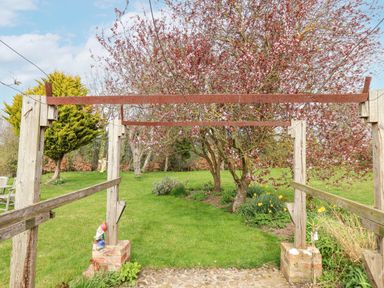 A garden with green grass and flowering trees viewed through a wooden pergola frame at The Barn - Poplar Farm in Lower Dunsforth near Boroughbridge