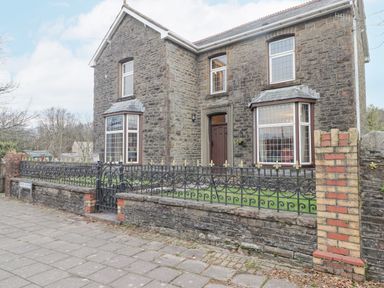 The exterior of a stone house with bay windows and a black wrought iron fence in front at Glan Yr Afon in Ystradgynlais