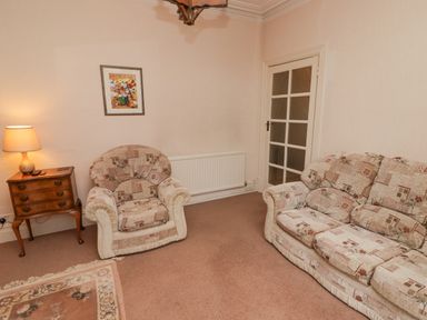 A living room with patterned armchair and sofa a wooden side table with lamp and a painting on the wall at Glan Yr Afon in Ystradgynlais