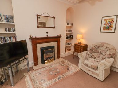 A living room with a fireplace a patterned armchair a lamp on a wooden side table and a television on a glass stand at Glan Yr Afon in Ystradgynlais