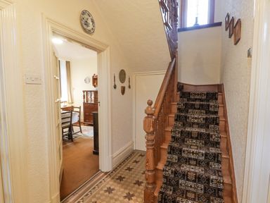 A hallway with wooden staircase and patterned carpet leading upstairs at Glan Yr Afon in Ystradgynlais