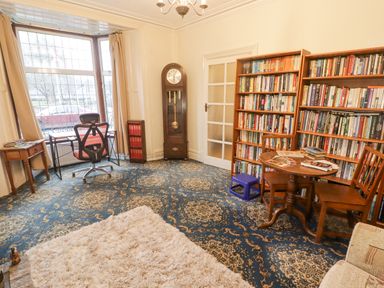 A room with bookshelves a round table with chairs a clock a desk and a chair at Glan Yr Afon in Ystradgynlais