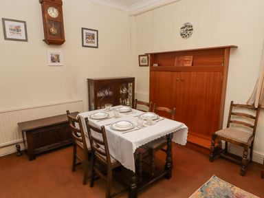 A dining room with a table set for four surrounded by wooden chairs and cabinets on the walls at Glan Yr Afon in Ystradgynlais