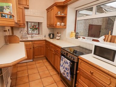 A kitchen with wooden cabinets tiled floor oven microwave and sink at Glan Yr Afon in Ystradgynlais