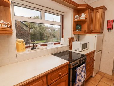 A kitchen with wooden cabinets a stove microwave and refrigerator near a window at Glan Yr Afon in Ystradgynlais