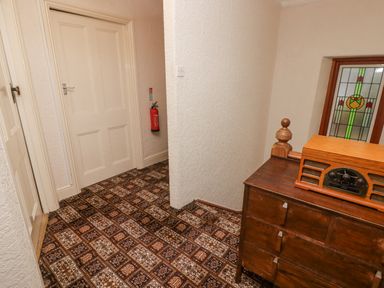 A hallway with patterned carpet a wooden chest of drawers and a fire extinguisher on the wall at Glan Yr Afon in Ystradgynlais