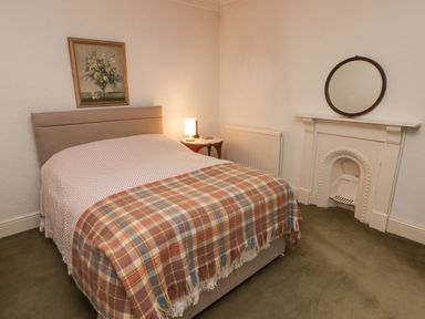 A bedroom with a bed a side table with a lamp a framed flower painting a fireplace with a round mirror and a green carpet at Glan Yr Afon in Ystradgynlais