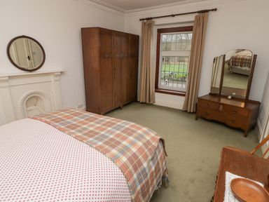 A bedroom with a bed a wooden wardrobe a dressing table with mirror a chair and a window with curtains at Glan Yr Afon in Ystradgynlais