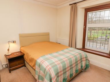 A bedroom with a double bed next to a window and a bedside table with a lamp at Glan Yr Afon in Ystradgynlais