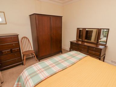 A bedroom with a bed, wooden wardrobe, dresser with mirror, chest of drawers, and a wooden chair at Glan Yr Afon in Ystradgynlais