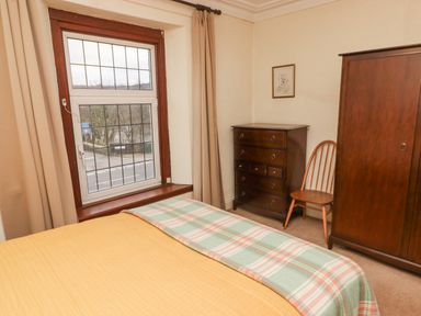 A bedroom with a bed covered by yellow and plaid blankets a window with grid patterns a wooden dresser a wooden chair and a wardrobe at Glan Yr Afon in Ystradgynlais