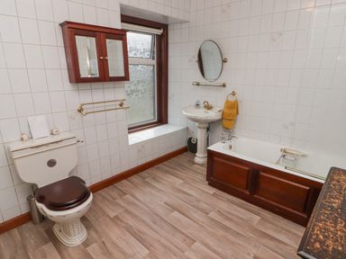 A bathroom with a toilet sink bathtub wooden cabinet and a window at Glan Yr Afon in Ystradgynlais