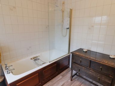 A bathroom with a bathtub with a showerhead and a dark wooden cabinet with drawers at Glan Yr Afon in Ystradgynlais