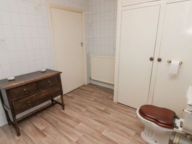 A bathroom with a wooden toilet seat a wooden cabinet a radiator and two closed doors at Glan Yr Afon in Ystradgynlais