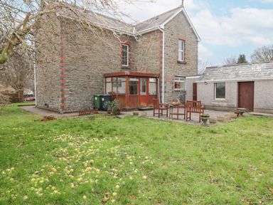 A stone house with a patio area that has wooden chairs and a table and a grassy garden with fallen apples at Glan Yr Afon in Ystradgynlais