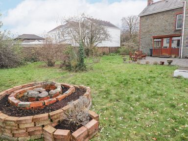 A backyard garden with brick plant beds grass and a patio area with benches at Glan Yr Afon in Ystradgynlais