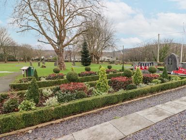 A garden with bushes and a memorial with wreaths in a park at Glan Yr Afon in Ystradgynlais