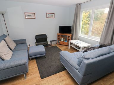 A living room with two blue sofas a small ottoman black rug TV on stand and large window at Kittiwake Apartment 22 Little Haven near Broad Haven