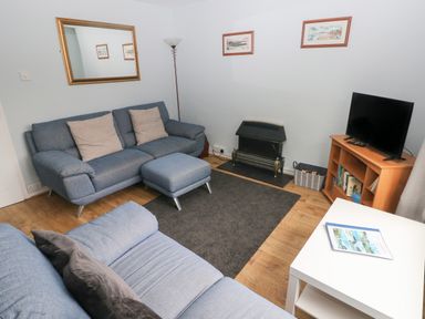 A living room with blue sofas a black fireplace a television on a wooden stand and a white table at Kittiwake Apartment 22 in Little Haven near Broad Haven