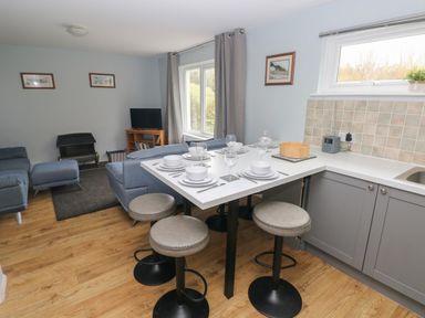 A kitchen and living area with a dining counter set with plates and glasses along with stools and blue sofas in a room at Kittiwake Apartment 22 in Little Haven near Broad Haven