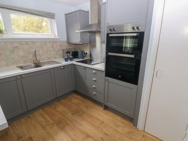 A kitchen with grey cabinets a double oven a stove sink and wooden floor at Kittiwake Apartment 22 in Little Haven near Broad Haven