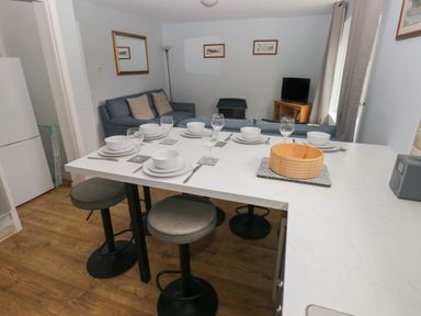A dining area with a set table on a countertop bar and a living room with a sofa and television in the background at Kittiwake Apartment 22 in Little Haven near Broad Haven