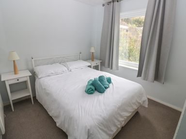 A bedroom with a double bed two bedside tables and lamps and a window with curtains at Kittiwake Apartment 22 Little Haven near Broad Haven