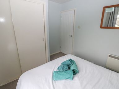 A bedroom with a bed holding four folded towels two white doors and a mirror on the wall at Kittiwake Apartment 22 in Little Haven near Broad Haven