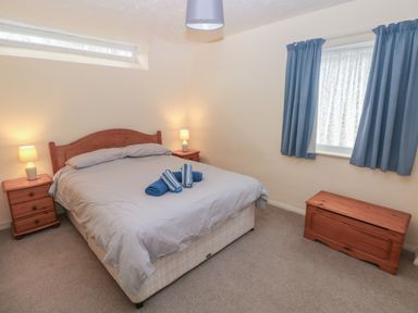 A bedroom with a double bed two bedside tables lamps blue curtains and a wooden chest at Kittiwake Apartment 22 in Little Haven near Broad Haven