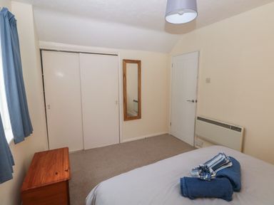 A bedroom with a bed folded towels a wooden chest a wall mirror and sliding door closet at Kittiwake Apartment 22 in Little Haven near Broad Haven
