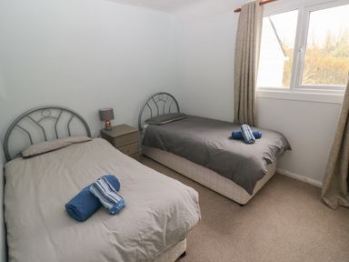 A bedroom with two single beds a bedside table with a lamp and a window with curtains at Kittiwake Apartment 22 in Little Haven near Broad Haven