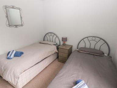 A bedroom with two single beds a nightstand with a lamp and a mirror on the wall at Kittiwake Apartment 22 in Little Haven near Broad Haven