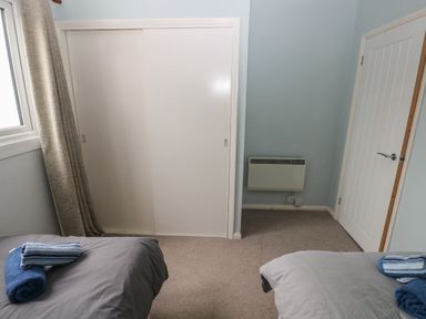 A bedroom with two beds with towels on them a closet with sliding doors a radiator and a door at Kittiwake Apartment 22 in Little Haven near Broad Haven