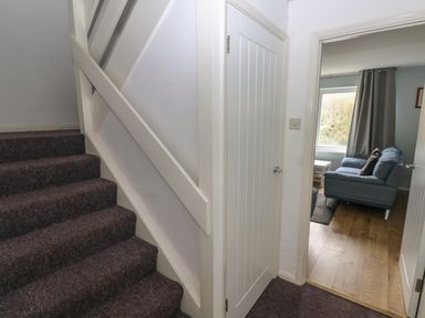A staircase with carpeted steps next to a white door and an open door showing a room with a blue sofa and wooden floor at Kittiwake Apartment 22 in Little Haven near Broad Haven