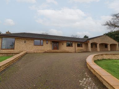 A stone building with a paved driveway and covered entrance at Blossom Hill near Witney