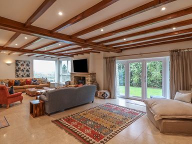 A living room with wooden beams on the ceiling a stone fireplace multiple sofas a patterned rug and glass doors opening to a garden at Blossom Hill near Witney
