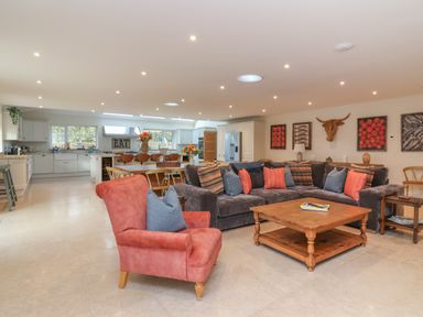 An open plan living and kitchen area with a large sectional sofa and a red armchair at Blossom Hill near Witney