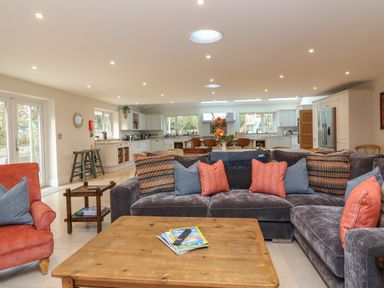 A living room with a large sectional sofa with cushions and a wooden coffee table with magazines and a remote at Blossom Hill near Witney