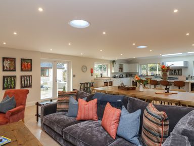 An open plan living room and kitchen with a gray sofa and pillows a wooden table and bar stools at Blossom Hill near Witney