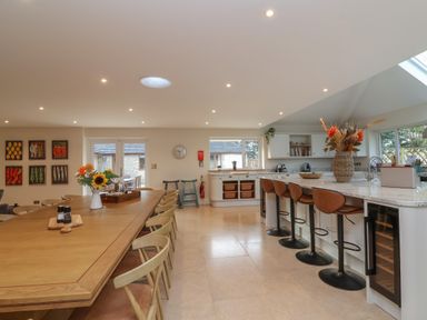 A kitchen with a large wooden dining table and chairs beside a marble island with bar stools at Blossom Hill near Witney