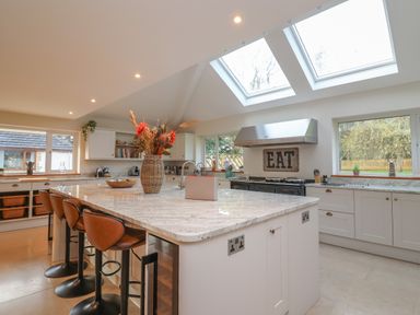 A kitchen with a large island and leather bar stools under skylights at Blossom Hill near Witney