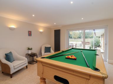 A game room with a pool table two armchairs and glass doors leading to an outdoor seating area at Blossom Hill near Witney
