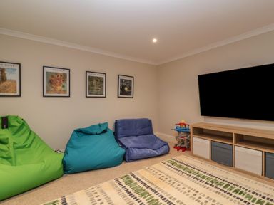 A room with three bean bag chairs a flat screen tv on a wooden stand framed pictures on the wall and a patterned rug at Blossom Hill near Witney